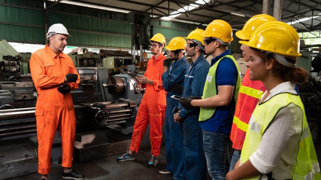 Instructor briefing a crew in hard hats and safety vests on a factory floor during an on-site safety class